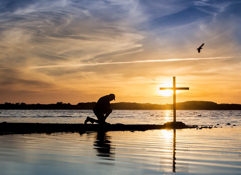 man kneeling prayer cross water